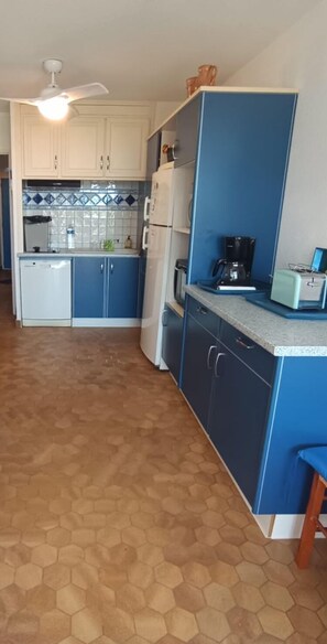 A compact kitchen with blue cabinets, a white refrigerator, a coffee maker, and a vintage toaster. - Beach and fishing at the end of the garden with private parking (La Grande-Motte)