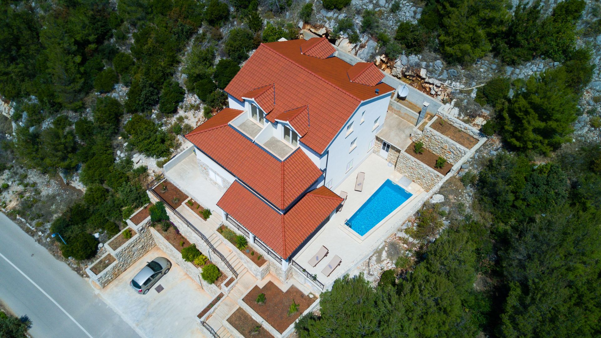 An aerial view of a two-story building with a red-tiled roof, a swimming pool, and a car parked in the driveway.