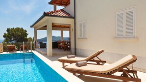 A pool area with lounge chairs and a covered seating area overlooking a scenic view.