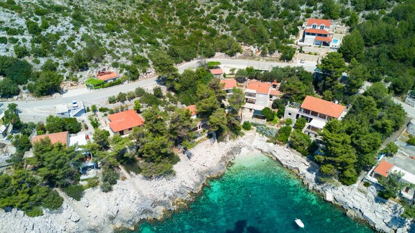 Vue aérienne d’un village côtier avec des bâtiments en pierre, une mer turquoise aux eaux limpides et une côte rocheuse.