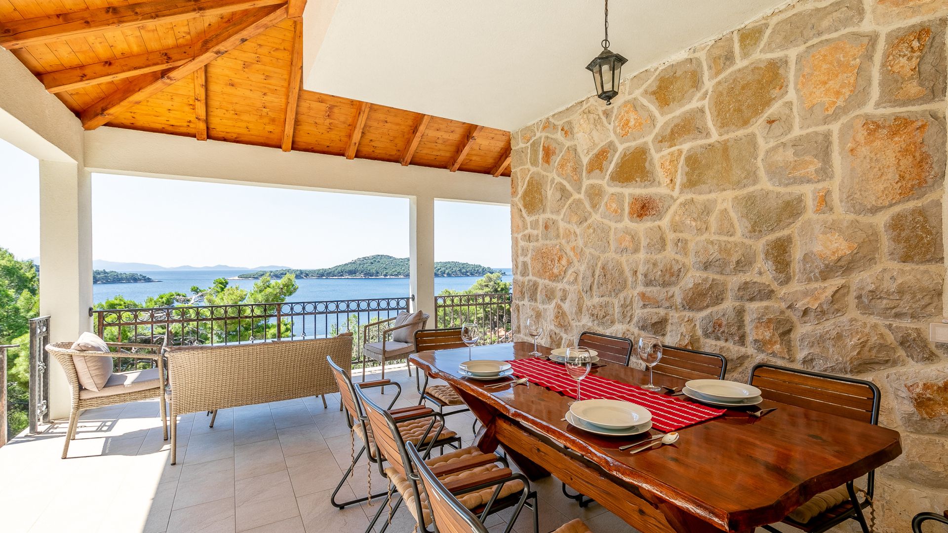 A dining area with a stone wall, wooden ceiling, and a view of the sea.