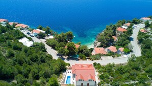 An aerial view of a coastal residential area with houses, a winding road, and a clear blue sea.
