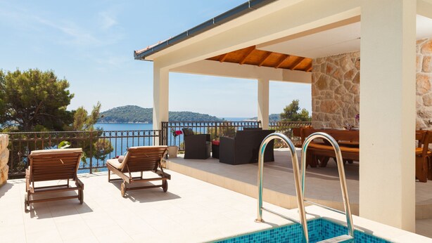 A covered outdoor area with a pool, lounge chairs, and a view of the sea.