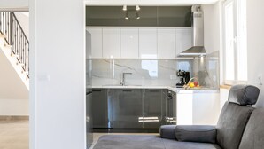 A modern kitchen with white cabinets, a stainless steel range hood, and a coffee machine.