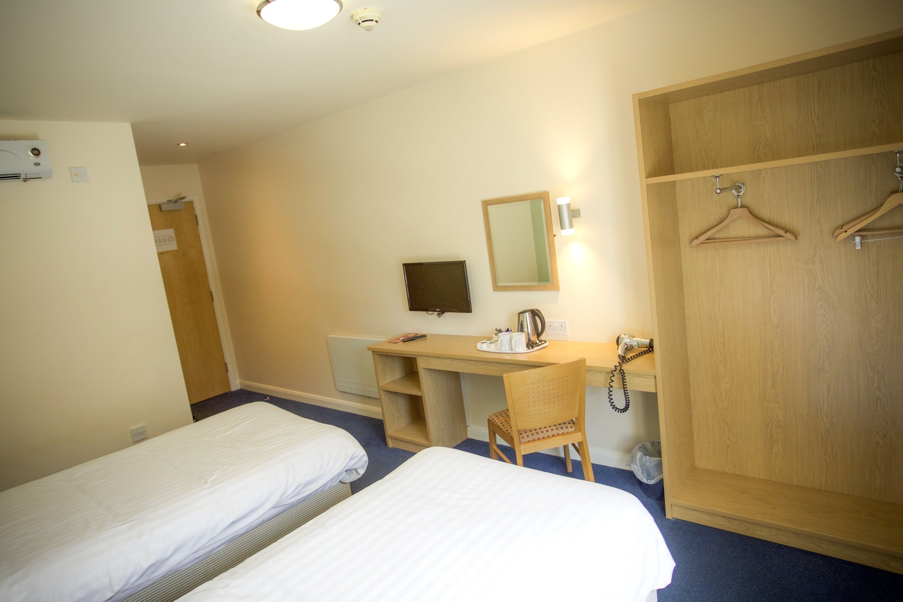 A hotel room with two single beds, a desk with a chair, a mirror, a wardrobe, and a telephone.