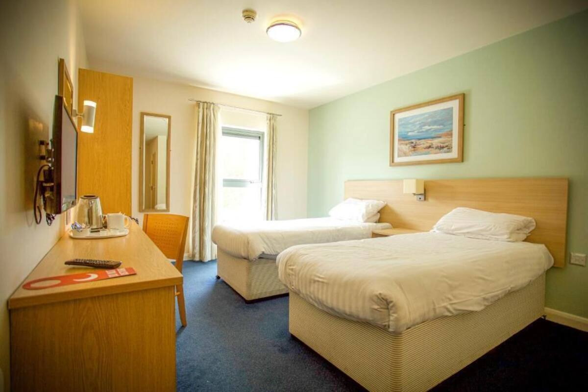 A hotel room with two beds, a desk, a chair, a coffee maker, and a painting on the wall.