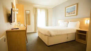 Een hotelkamer met een bed, een bureau, een stoel, een kledingkast en een schilderij aan de muur.