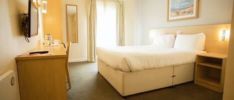 A hotel room with a bed, a desk, a chair, a wardrobe, and a painting on the wall.