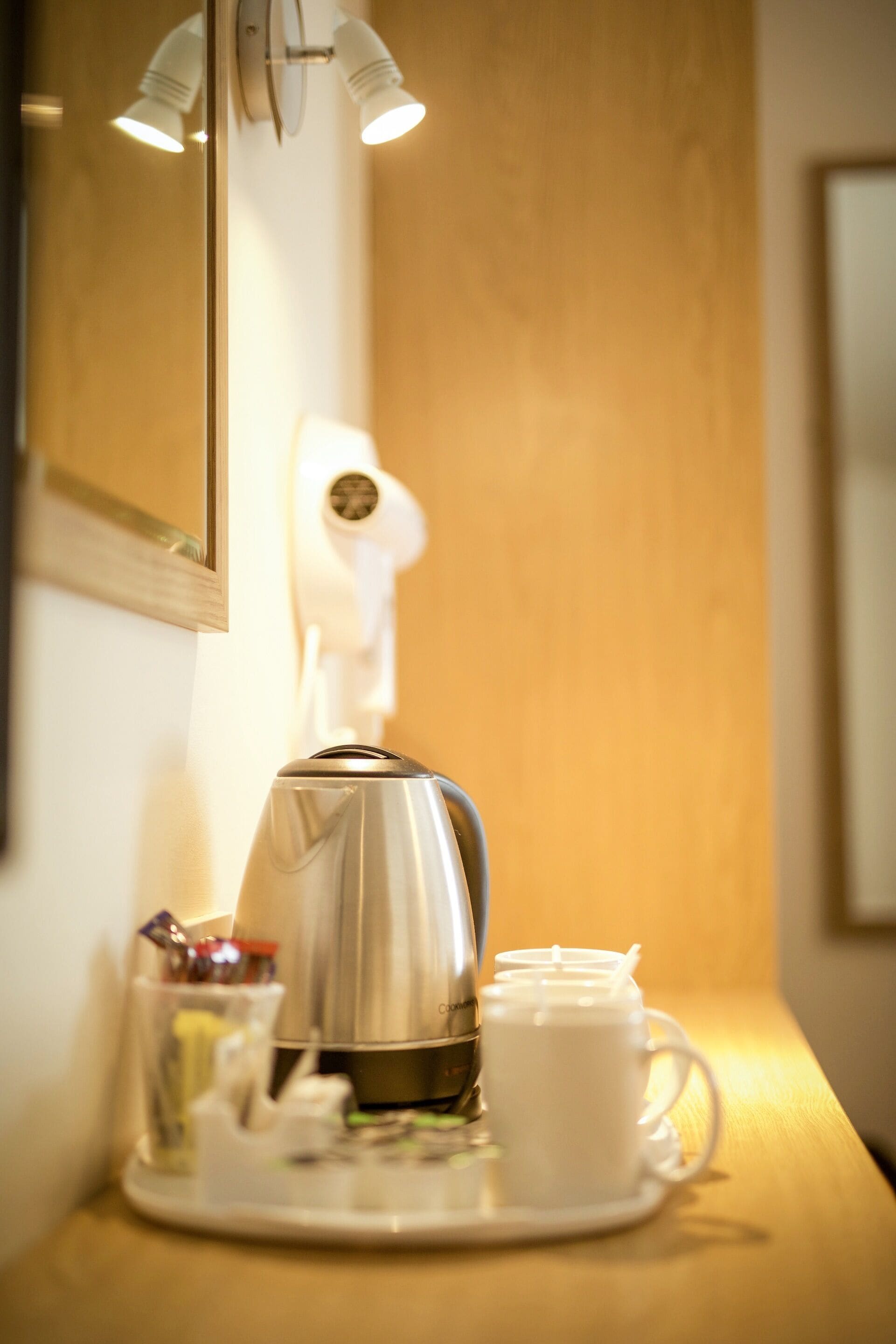 A coffee maker on a tray with a cup and saucer, a glass of water, and a small container with utensils on a wooden counter.