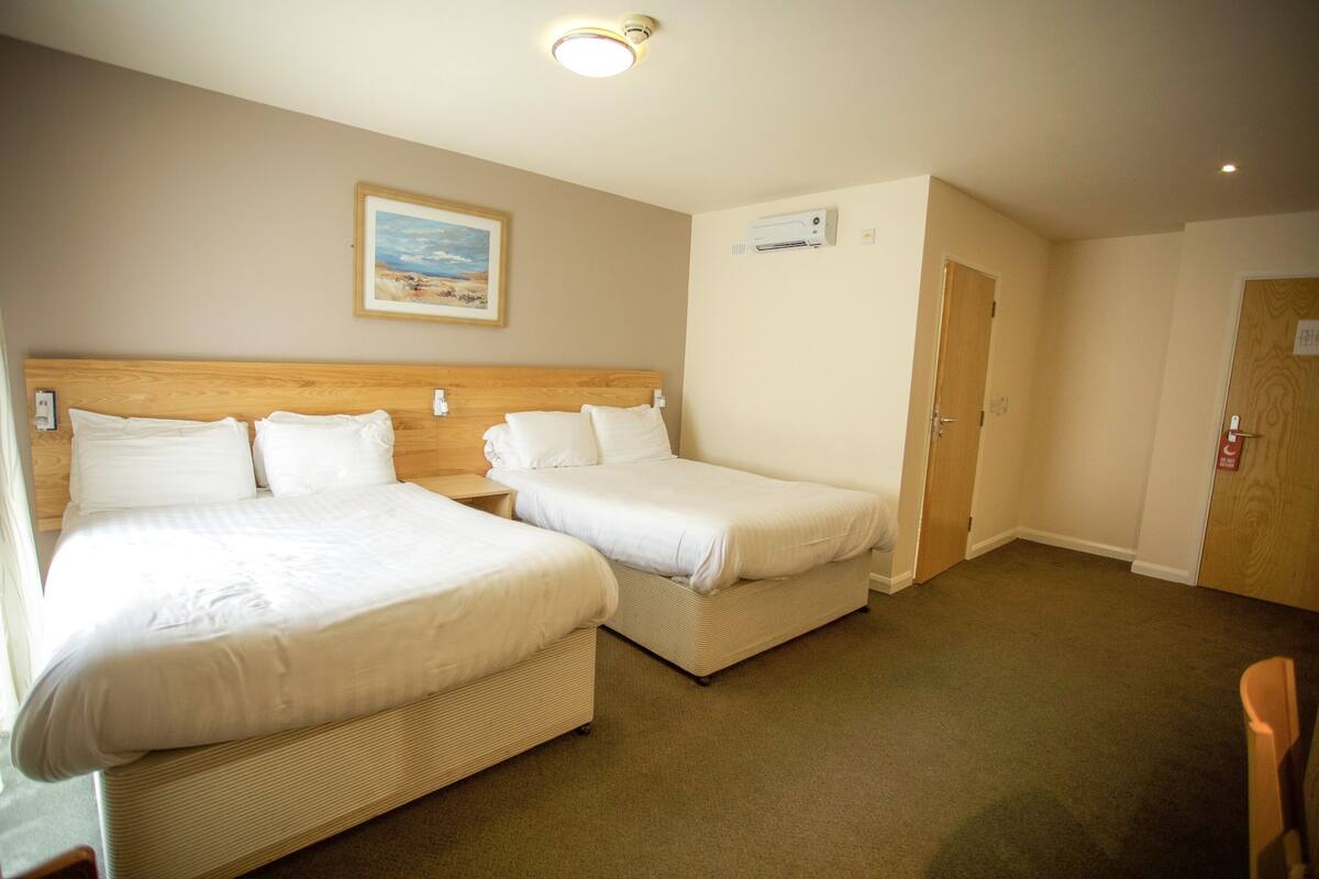 A hotel room with two single beds, a wooden headboard, a framed picture on the wall, an air conditioning unit, and a door with a number sign.