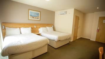 Habitación de hotel con dos camas individuales, cabecera de madera, un cuadro enmarcado en la pared, equipo de aire acondicionado y una puerta con un letrero de número.