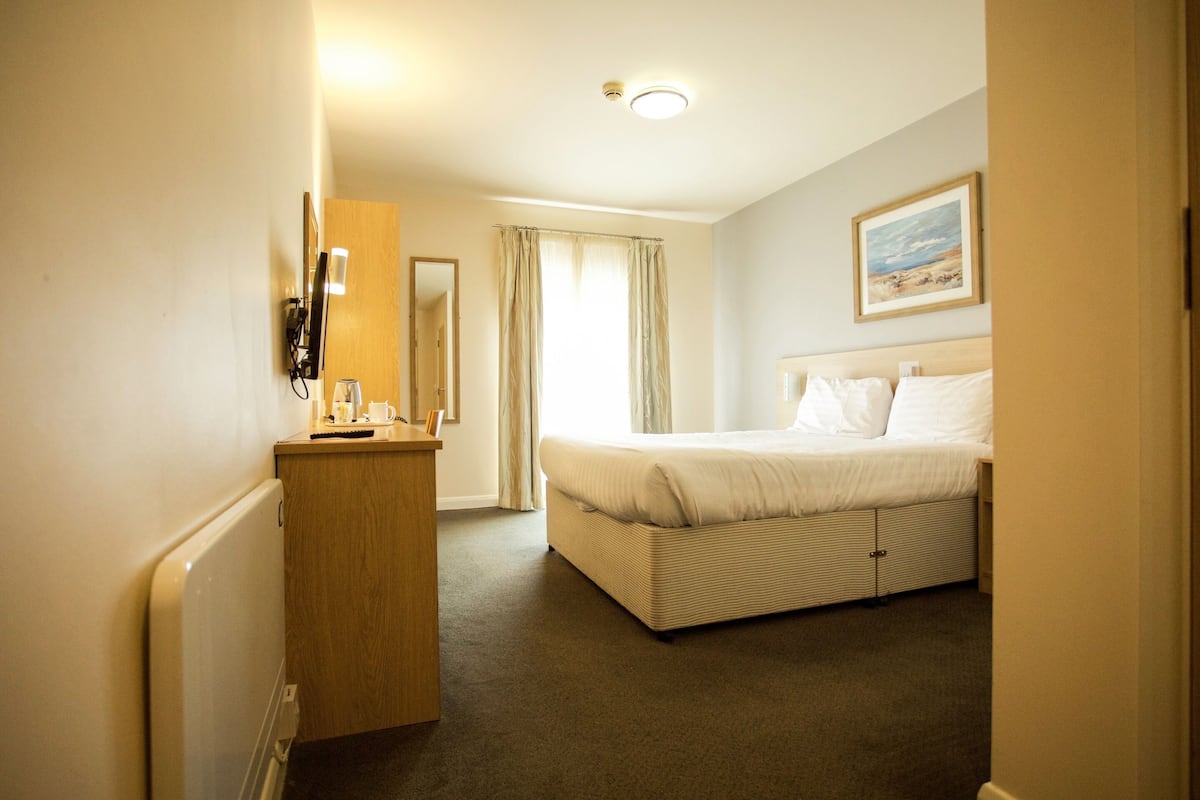 A hotel room with a bed, a dresser, a mirror, and a painting on the wall.