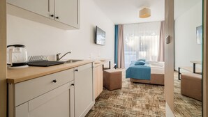 A modern hotel room with a kitchenette, a bed with a blue blanket, and a large window with sheer curtains. - Apartamenty Sun & Snow Welle Resort (Grzybowo)