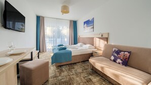 A hotel room with a bed, a sofa, a desk with a chair, and a TV mounted on the wall. - Apartamenty Sun & Snow Welle Resort (Grzybowo)