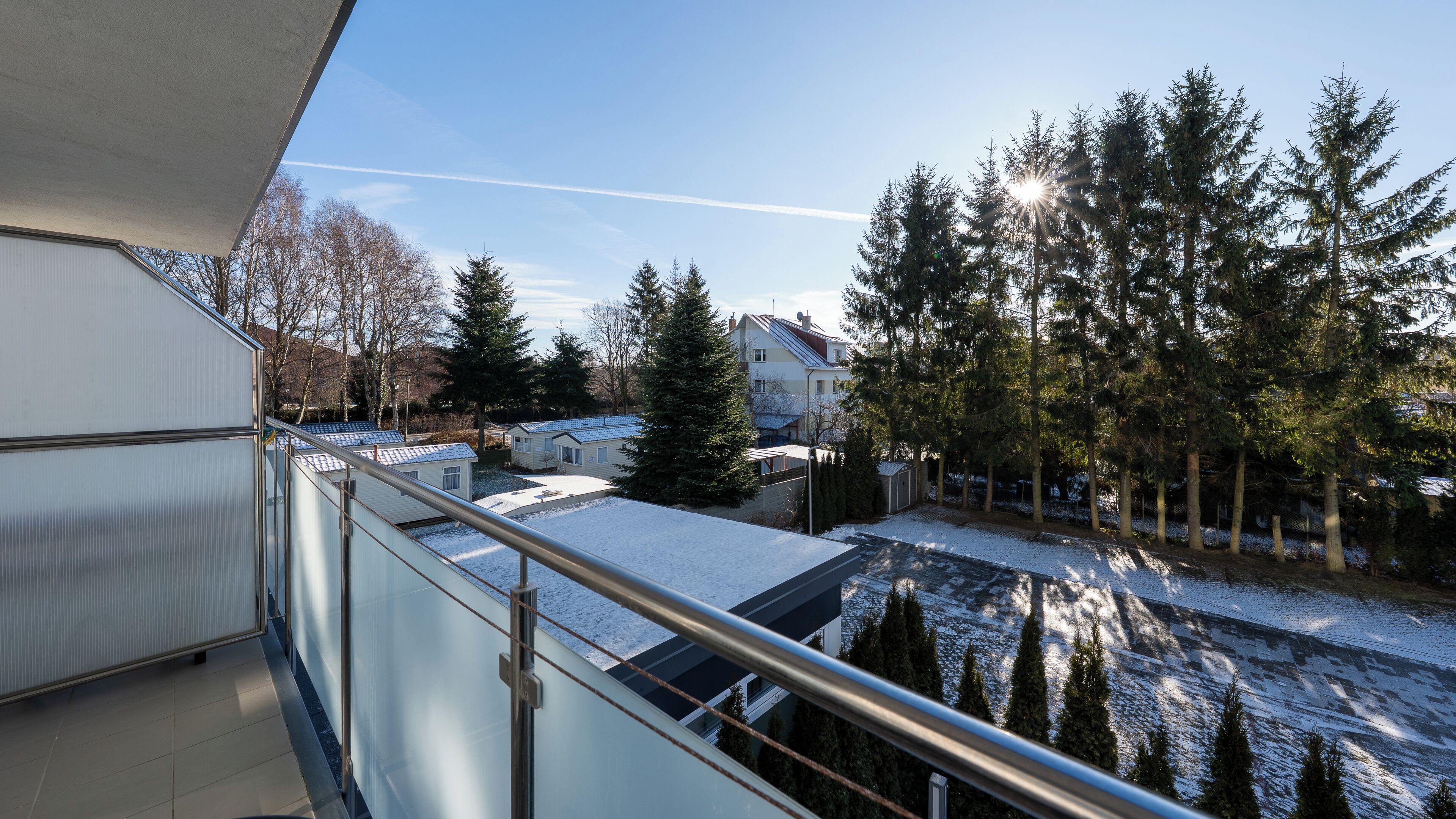 A residential area with snow-covered ground, houses, and tall evergreen trees.