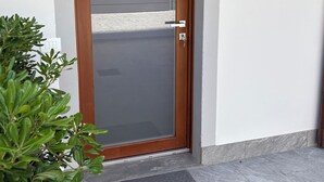 Une porte en bois avec un panneau de verre, un paillasson sur lequel est écrit « Chez soi, quel bonheur ! », et une plante en pot à côté.