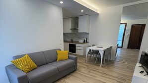 Un appartement moderne avec un canapé gris, des coussins jaunes, un coin repas et une cuisine.