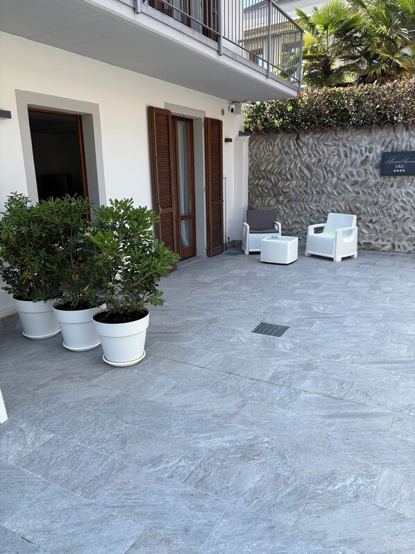 A modern outdoor patio area with potted plants, white wicker furniture, and a stone wall.