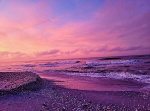 En strand med bølger, sten og en solnedgang.