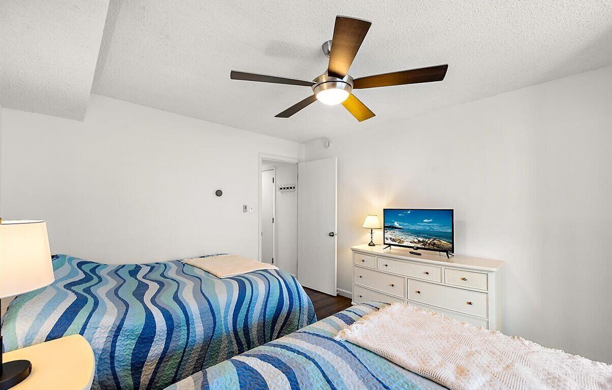 A bedroom with two beds, a ceiling fan, a TV, and a dresser.