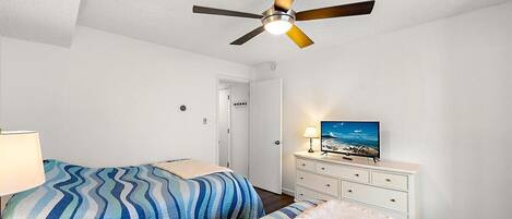 A bedroom with two beds, a ceiling fan, a TV, and a dresser.