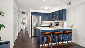 A modern kitchen with dark blue cabinets, stainless steel appliances, and a central island with bar stools. - Close to the Boardwalk, Jolly Roger Amusement Park and All the OC Fun! (Ocean City)