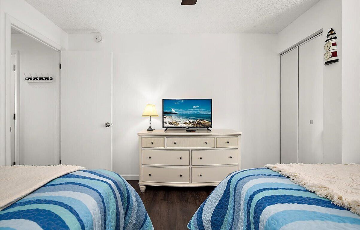Un dormitorio con dos camas, un tocador, un televisor y un reloj en la pared.