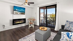 A modern living room with a fireplace, a ceiling fan, a large window with a view of the outside, and a grey sofa with patterned cushions. - Close to the Boardwalk, Jolly Roger Amusement Park and All the OC Fun! (Ocean City)