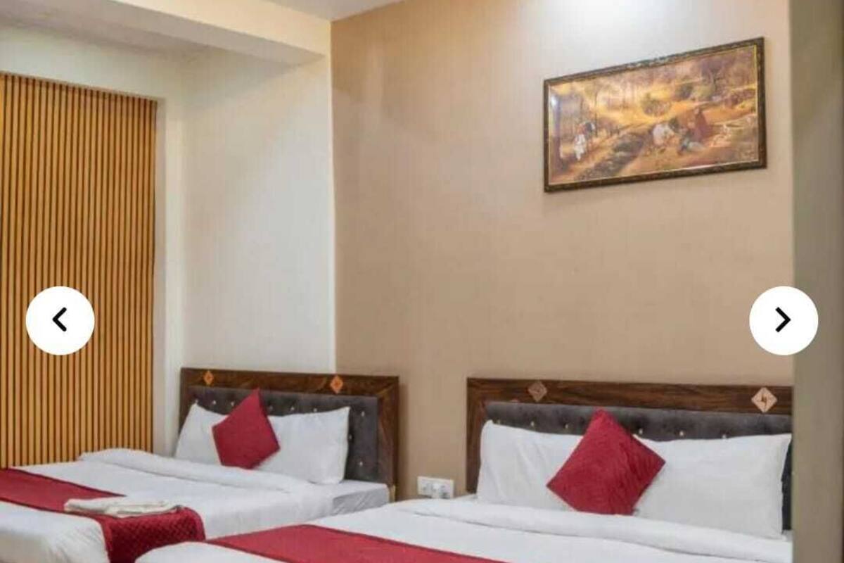 Habitación de hotel con dos camas, cabeceros de madera, ropa de cama blanca, detalles en rojo, ventilador de techo, iluminación empotrada y un cuadro en la pared.