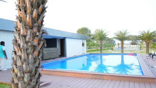 Une piscine avec une terrasse en bois, des palmiers et un bâtiment moderne dont la porte est ouverte.