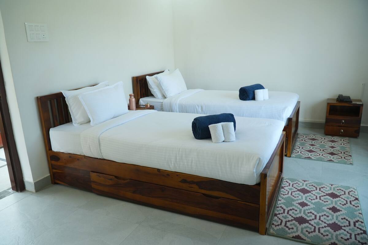 Une chambre d’hôtel avec deux lits en bois, du linge de lit blanc et une petite table de chevet en bois avec un téléphone.
