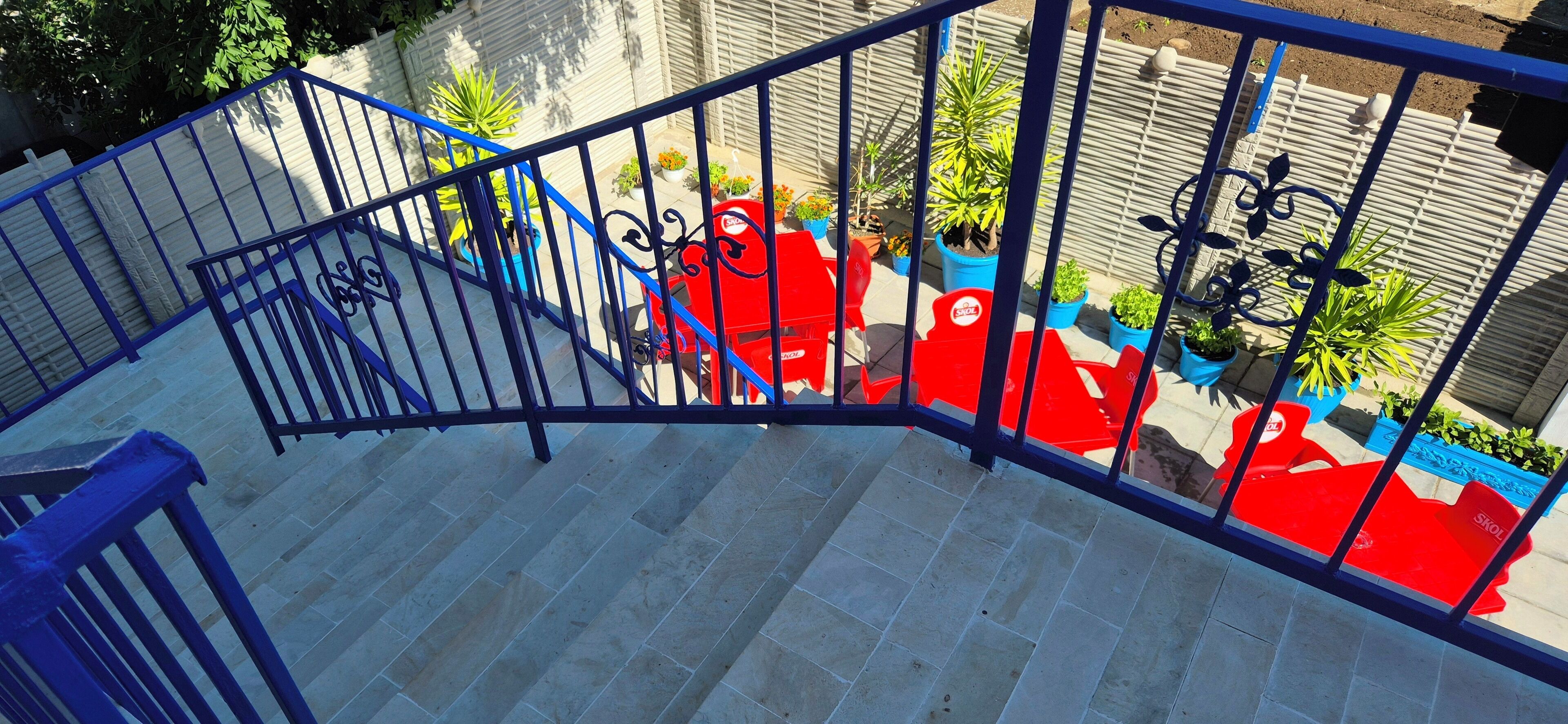 Un escalier avec des rampes bleues menant à un balcon agrémenté de plantes en pot et de chaises rouges.