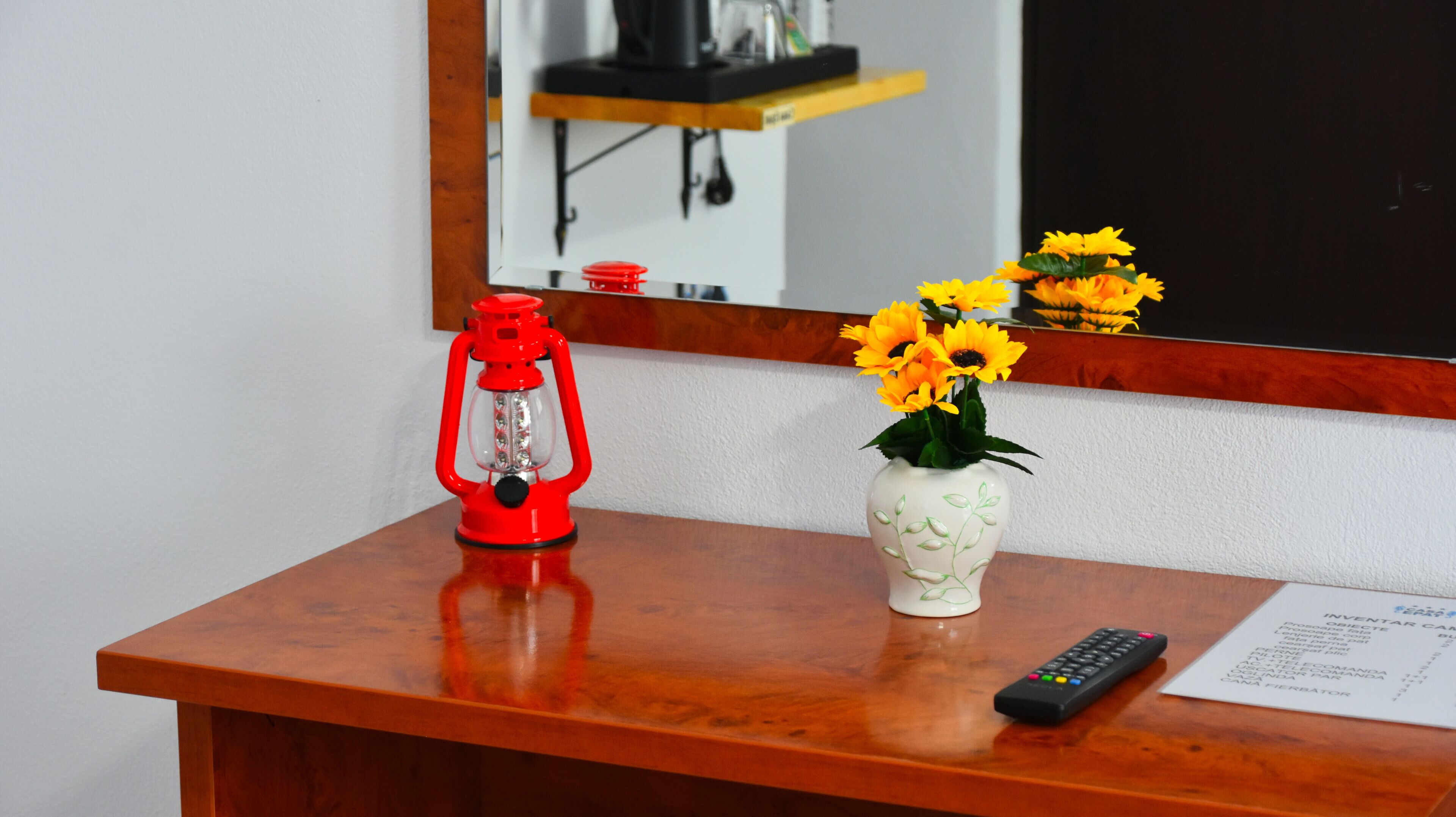 Un escriptori de fusta amb un farol vermell, un vas amb flors grogues i un comandament a distància.