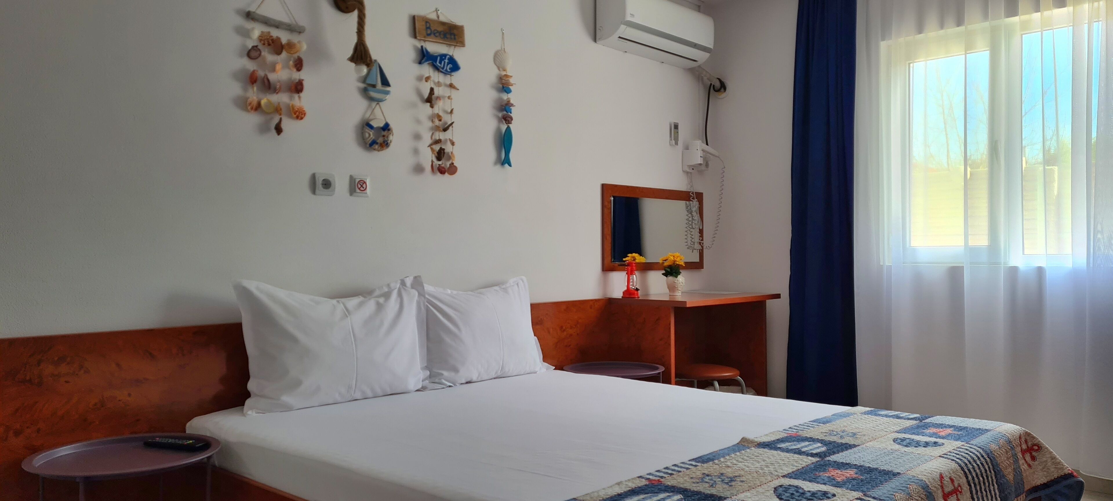 A hotel room with a bed, a small table, a mirror, and a window with curtains.