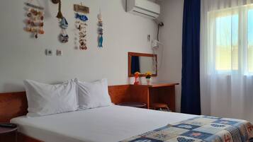 A hotel room with a bed, a small table, a mirror, and a window with curtains.