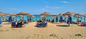 A beach with sun umbrellas and lounge chairs, a clear sky, and the ocean in the background.