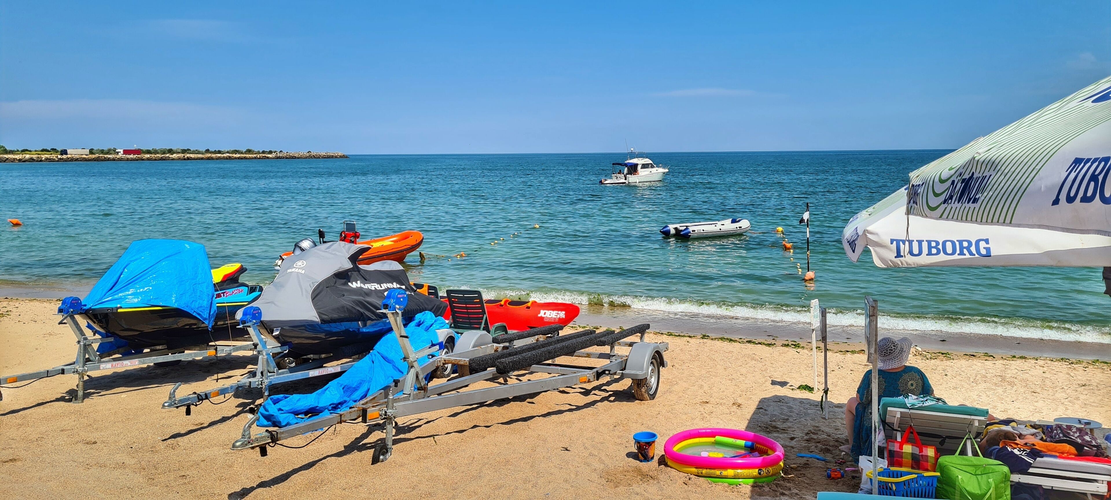 Une plage avec une remorque pour bateau, des bateaux gonflables et un parasol Tuborg.