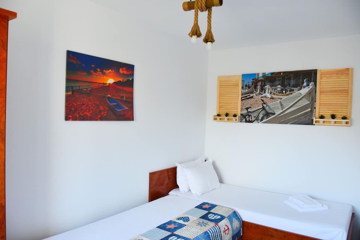 A neatly made bed with a quilt, a wooden headboard, and a wall-mounted picture of a sunset over a beach.