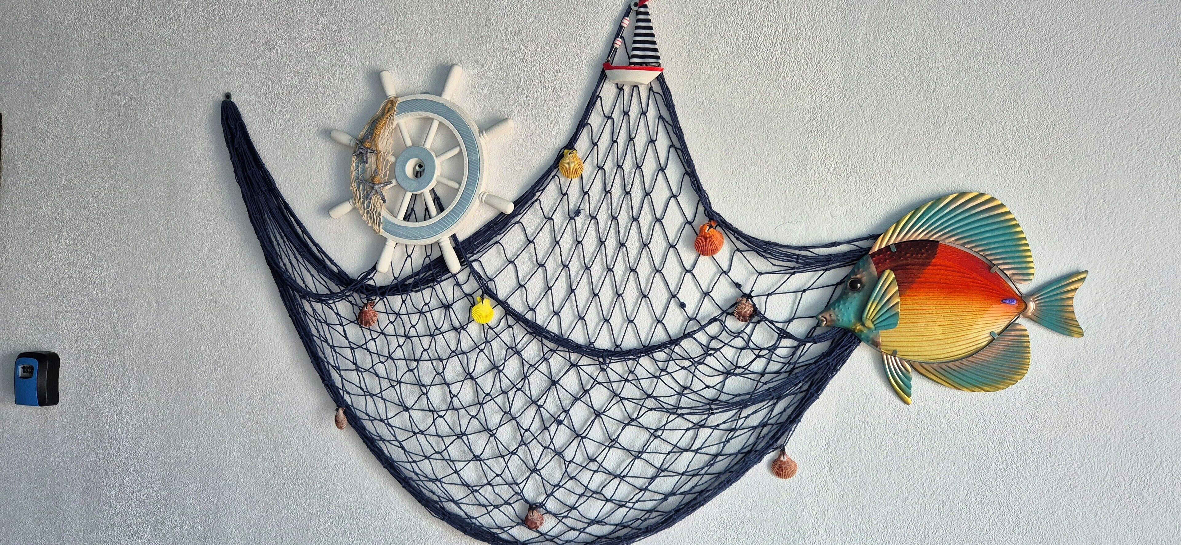 A hammock with a net, a ship's wheel, and a fish decoration on a textured wall.