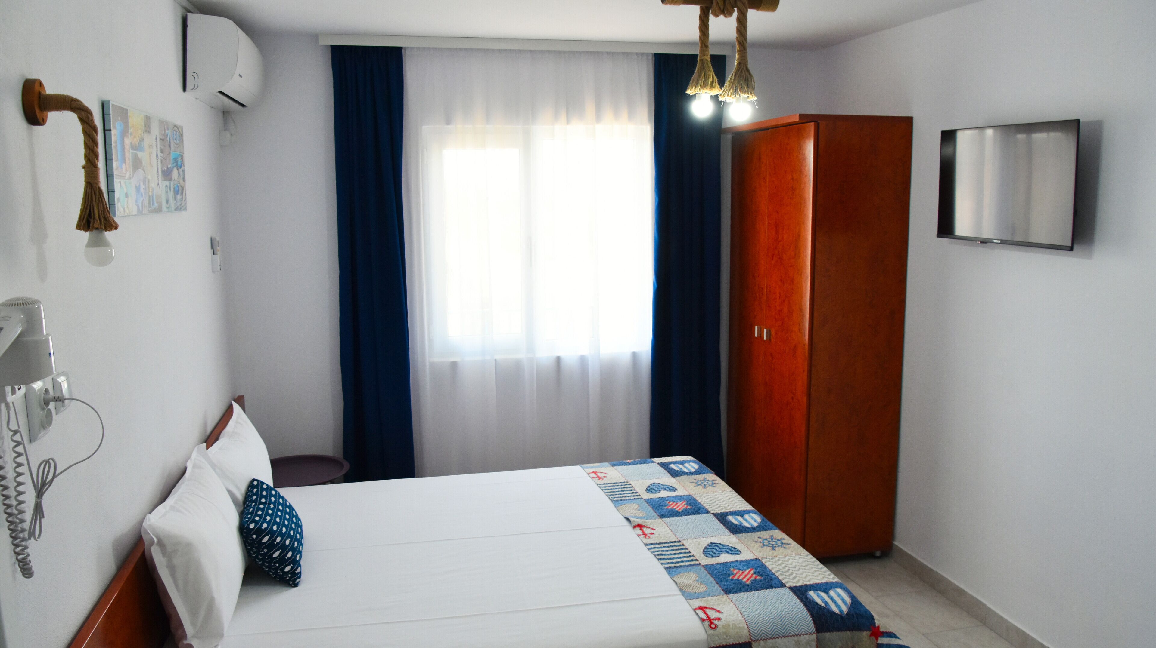 Une chambre d’hôtel avec un lit, une armoire, un téléviseur fixé au mur et une fenêtre avec des rideaux.
