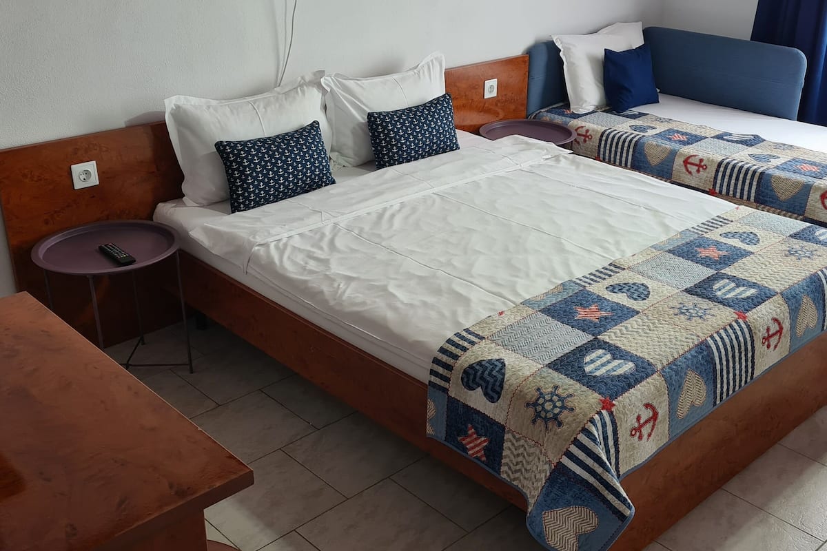 A hotel room with two beds, a wooden table, a small round table, and a nightstand with a lamp.