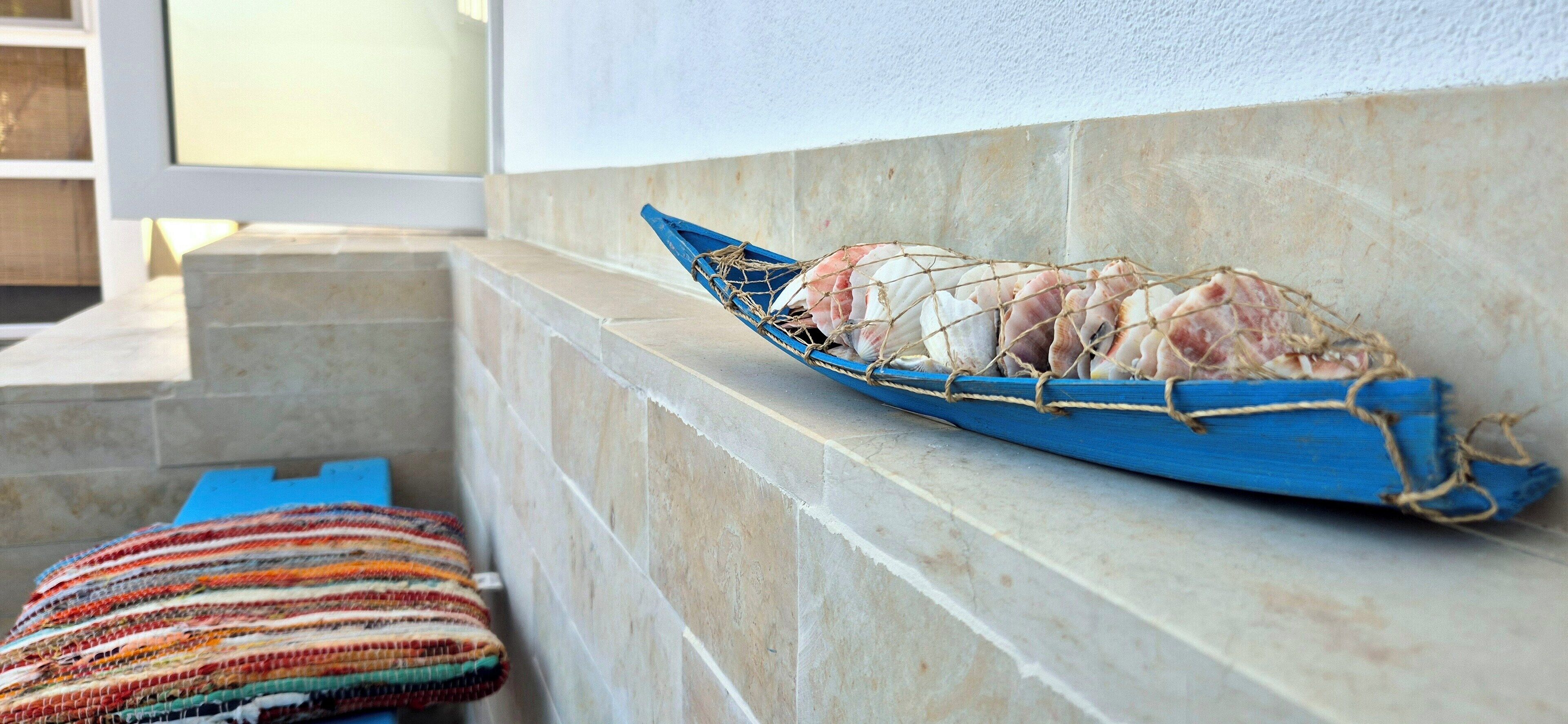 A blue boat filled with seashells and tied to a stone wall.
