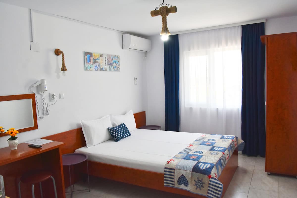 A hotel room with a bed, a desk with a chair, a wardrobe, and a window with curtains.