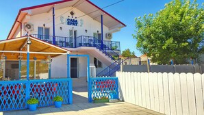 A two-story building with a blue balcony, a covered outdoor seating area, and a white picket fence. - EPAT  (Limanu)