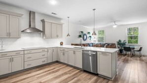 A modern kitchen with white cabinetry, a stainless steel dishwasher, and a dining area with a table and chairs. - 2BR | 2BA Close to Beach, Luxury Amenities + Free Tix: Dolphin Cruise & More! (Santa Rosa Beach)