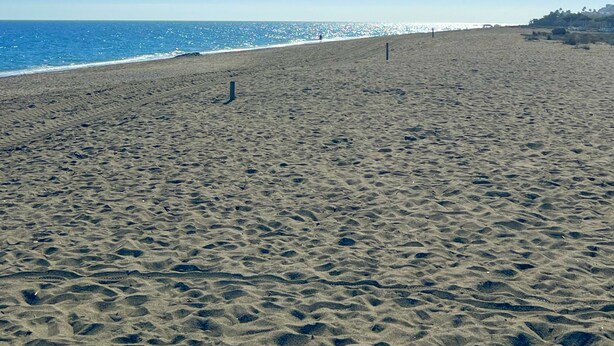 Une vaste plage de sable fin, avec un ciel dégagé et l’océan en toile de fond.