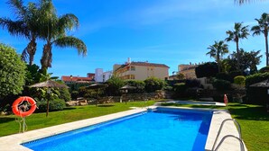 Une piscine à l’eau d’un bleu cristallin, entourée d’une terrasse en béton, de palmiers et d’une pelouse.