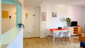 Un vaste espace de vie comprenant une table à manger, des chaises, un téléviseur et un fauteuil en osier.