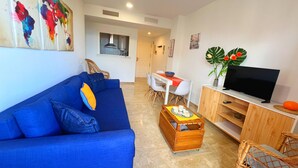 Un salon moderne avec un canapé bleu, un meuble TV en bois et un coin repas comprenant une table et des chaises.