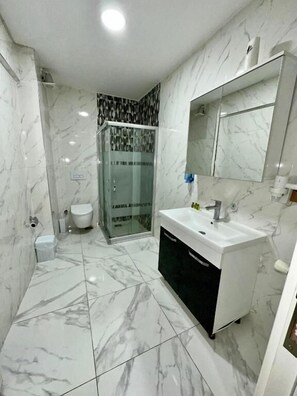 A modern bathroom with a marble floor, a white sink, a black cabinet, a glass shower enclosure, and a toilet. - avrasya queen hotel (İstanbul)